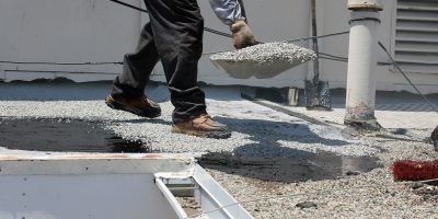 Unidentifiable workers use "Hot Tar" aka "Hot Mop" to lay down Molten Tar, Asphalt Sheets and Pea Gravel on a Flat roof on a Hot Summer day in Southern California. Roofs are important on houses; Shutterstock ID 208056592; purchase_order: -; job: -; client: -; other: -